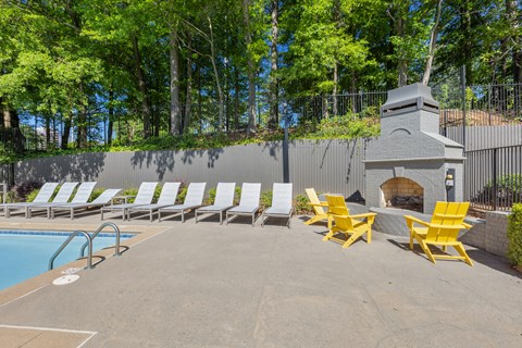 a pool with yellow lounge chairs next to a fireplace