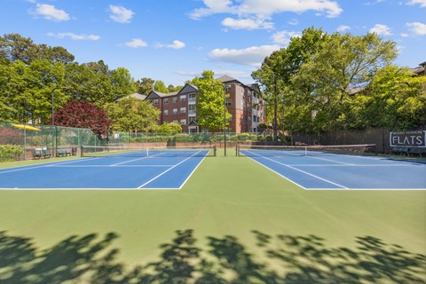 two tennis courts with a building and trees in the background