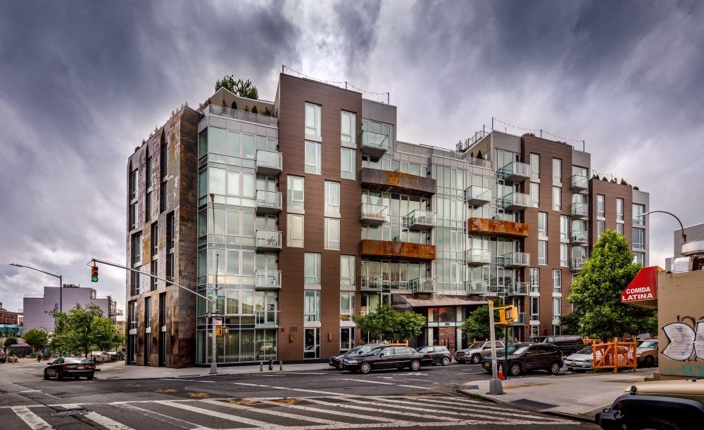 A modern multi-story building with a glass facade is situated on a busy street corner.