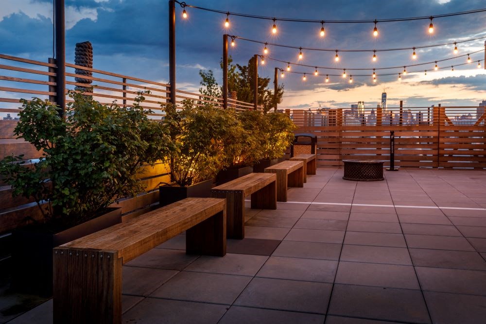 A rooftop patio with benches and string lights.