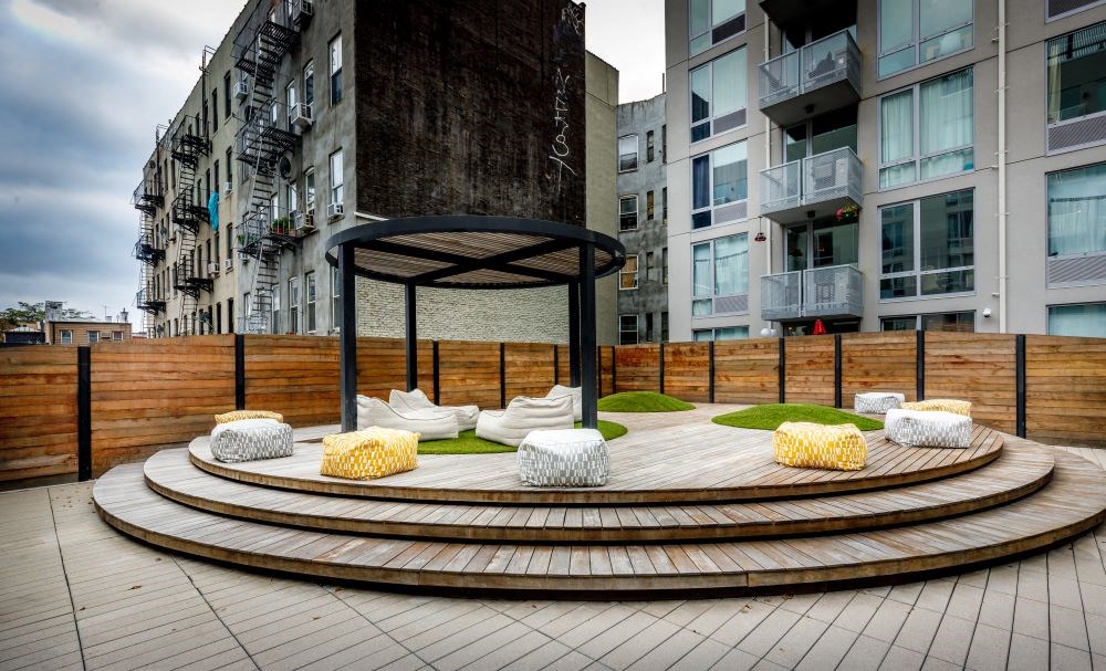 A patio with a black umbrella and white cushions.