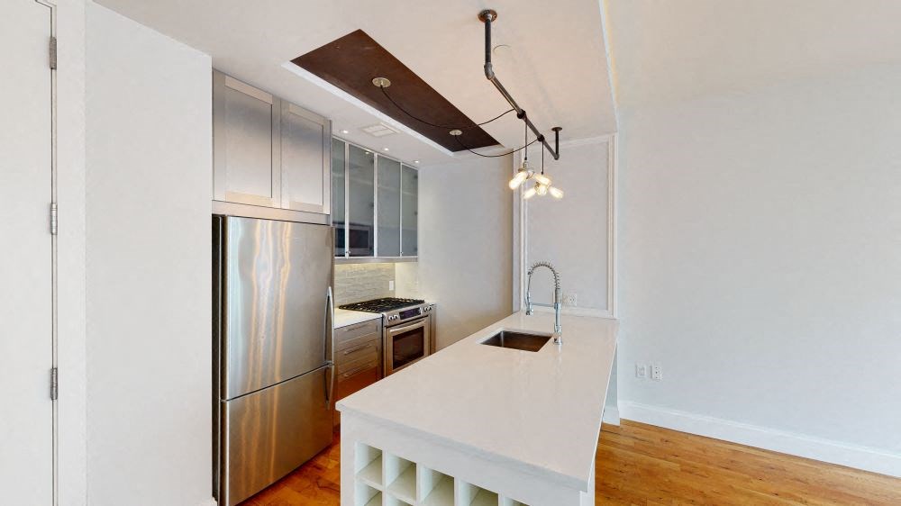 A modern kitchen with a stainless steel refrigerator and a white countertop.