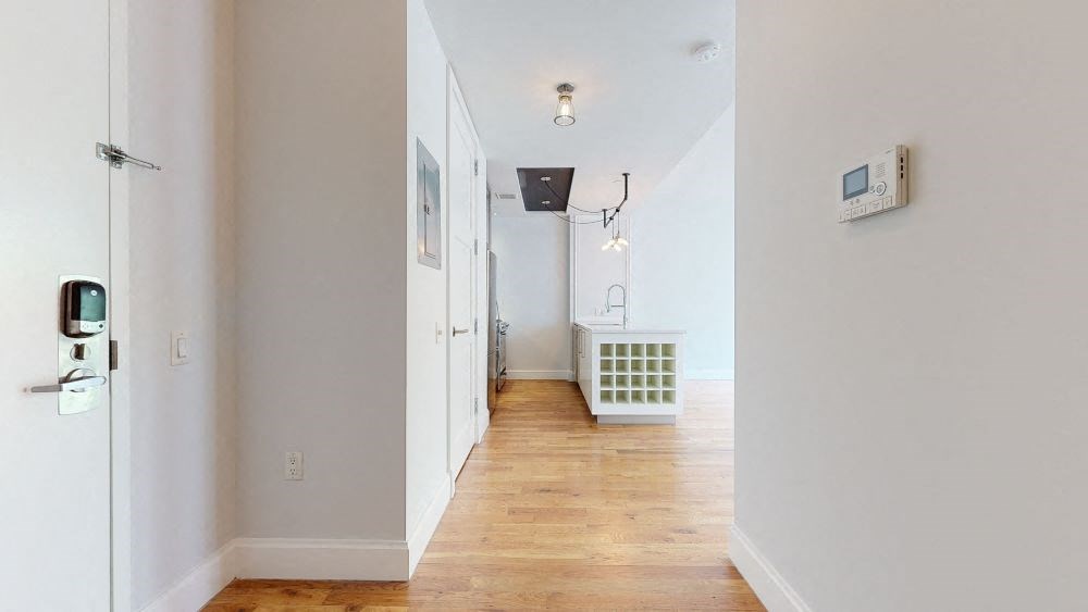 A long hallway with a door on the left and a thermostat on the wall.
