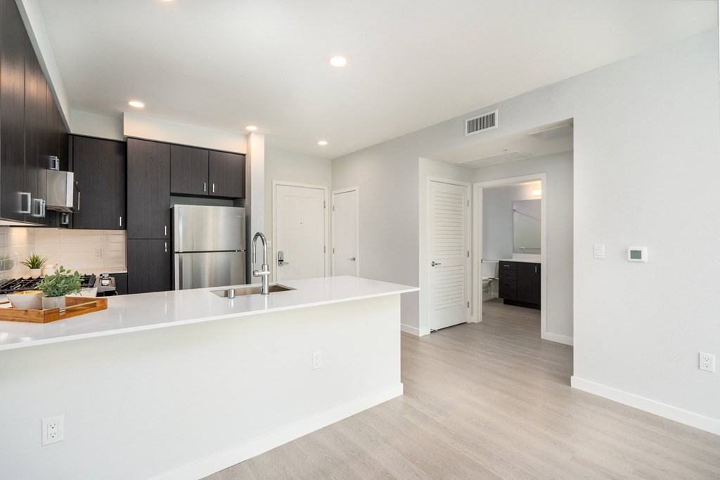 a white kitchen with a large island and a stainless steel refrigerator