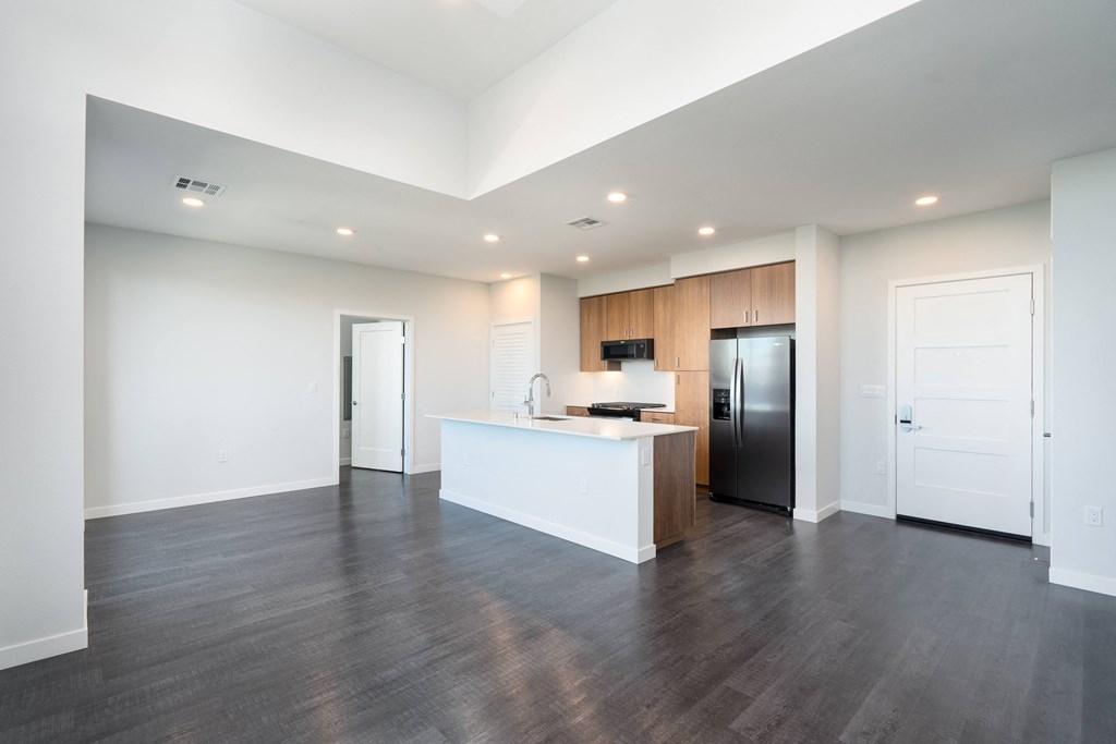 an empty living room with a kitchen and a refrigerator