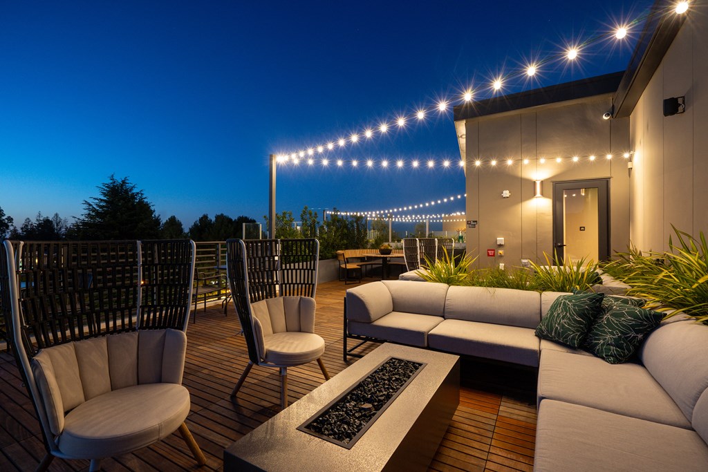 a roof deck with couches and chairs and a fire pit at night