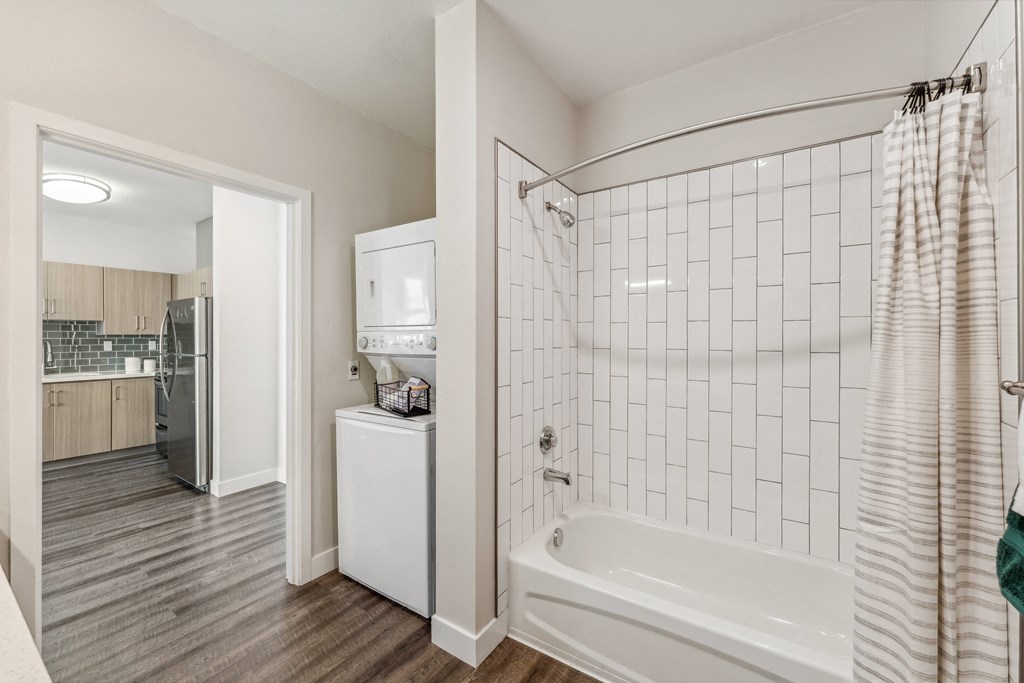 a white tiled bathroom with a tub and shower and a kitchen