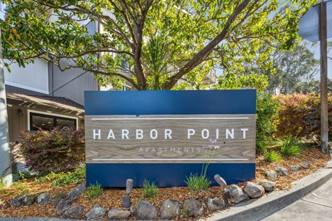 A sign that says Harbor Point Apartments in front of a tree.