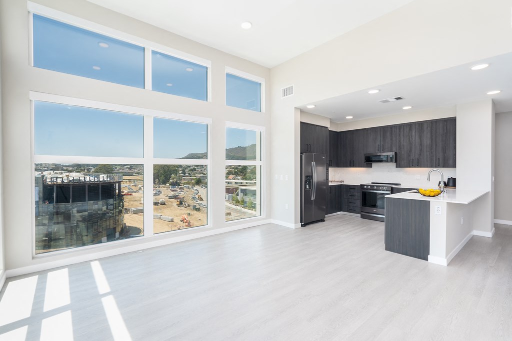 an empty living room with large windows and a kitchen