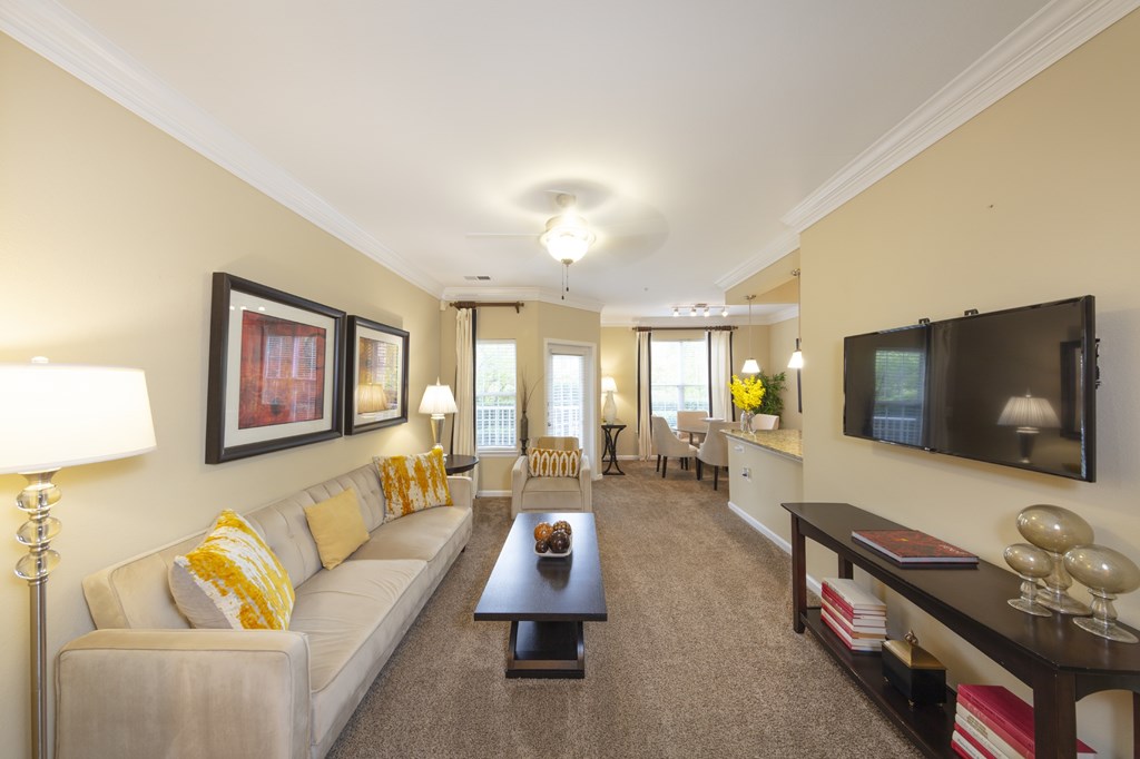 A well-lit living room with a white sofa, a coffee table, and a flat-screen TV mounted on the wall.