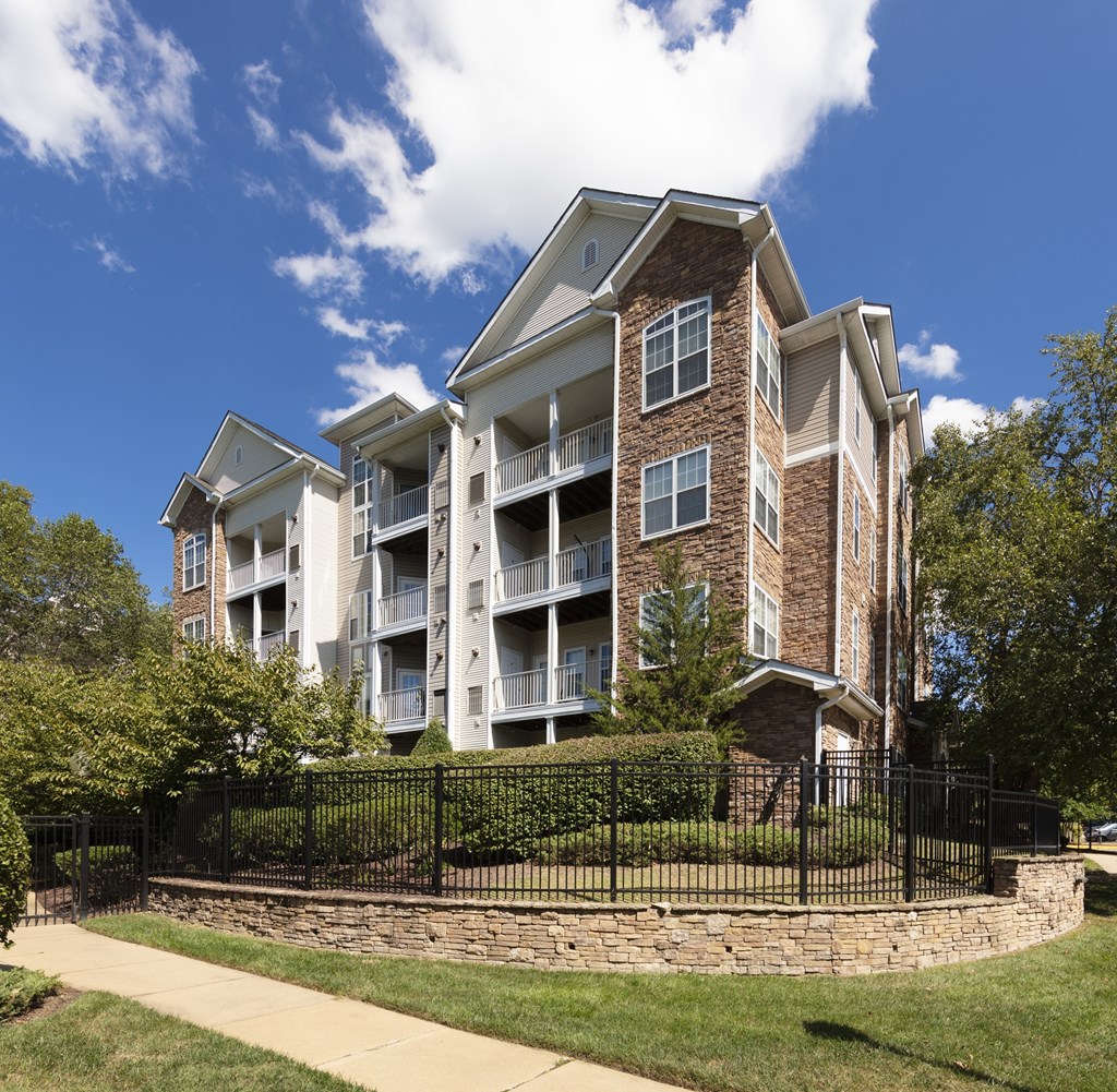 A large brick apartment building with a black fence and a stone wall.