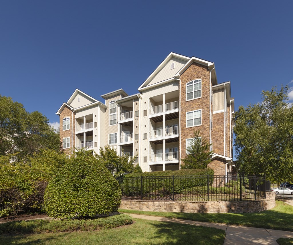 A large apartment building with a black fence and green bushes in front.