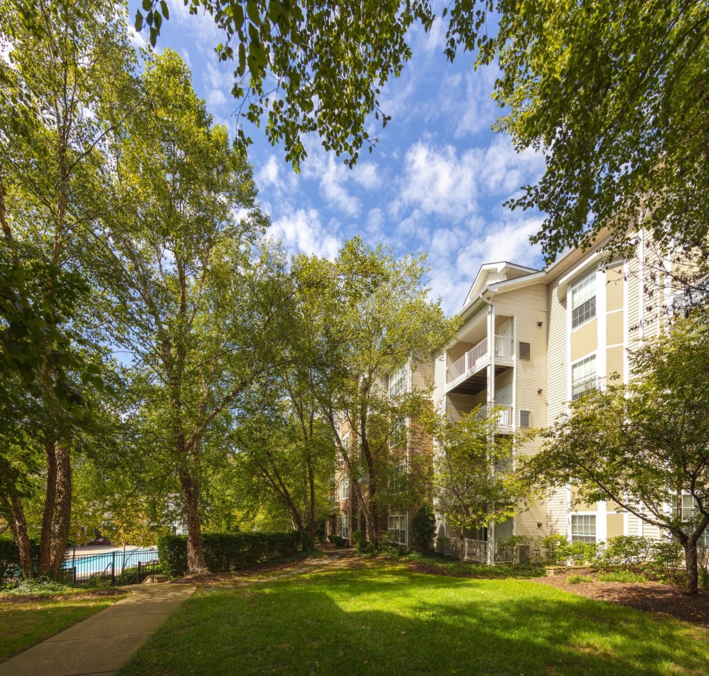 A tree-lined pathway leads to a large apartment building.