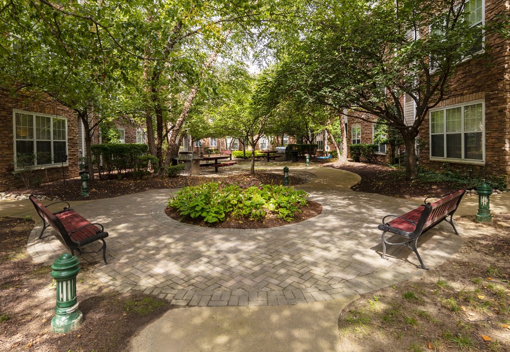 A courtyard with a circular brick walkway, benches, and trees.