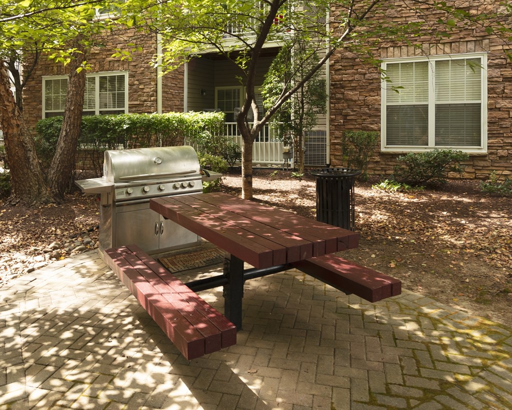 A picnic table with a grill is in front of a brick building.