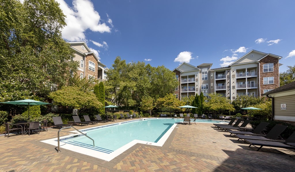 A swimming pool surrounded by lounge chairs and umbrellas in a sunny outdoor setting.