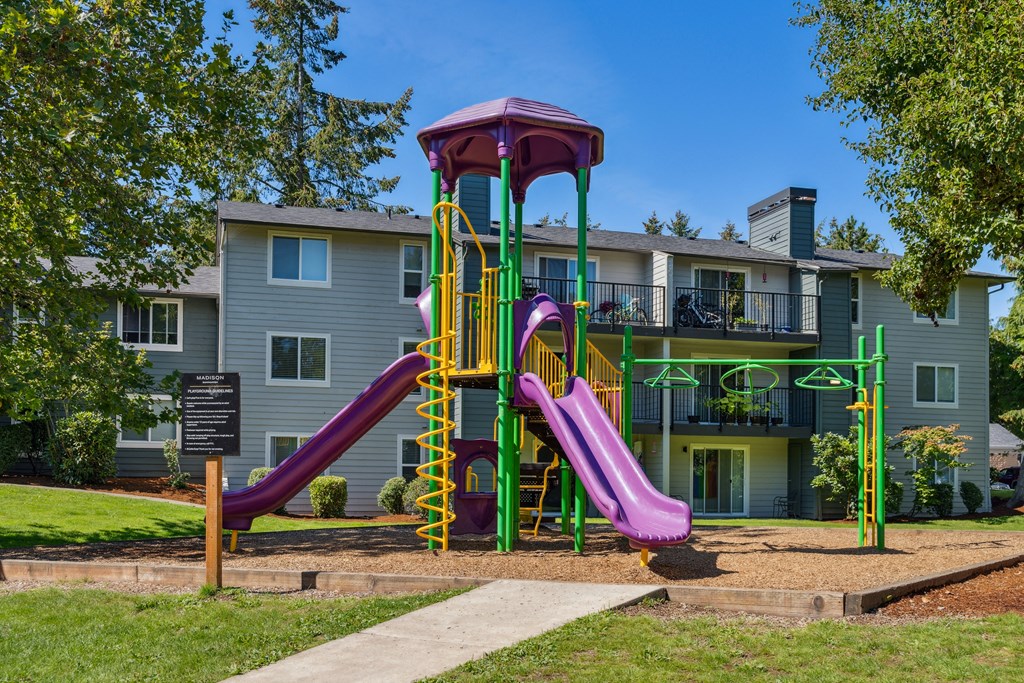 a playground with two slides in front of an apartment building