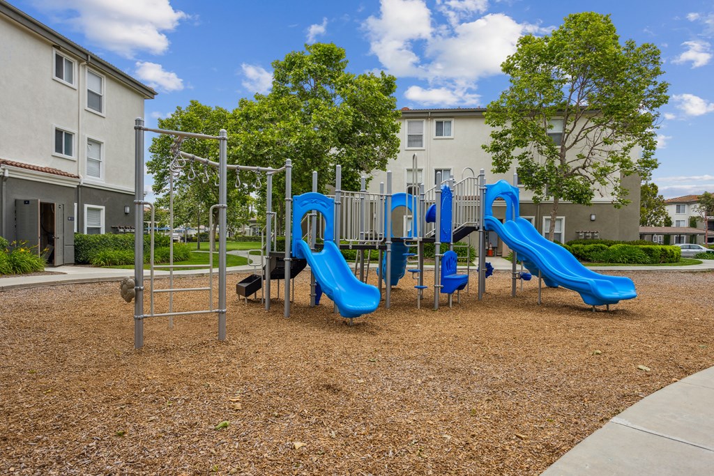 a playground with blue slides and swings at an apartment complex