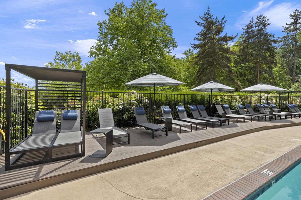 a pool with lounge chairs and umbrellas next to a fence