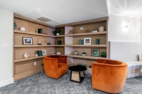 a living room with two orange chairs and a wall with wooden shelves