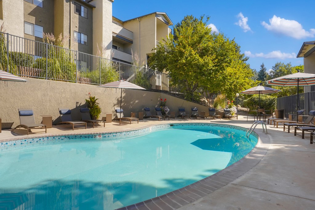 a swimming pool with chairs and umbrellas in front of a building