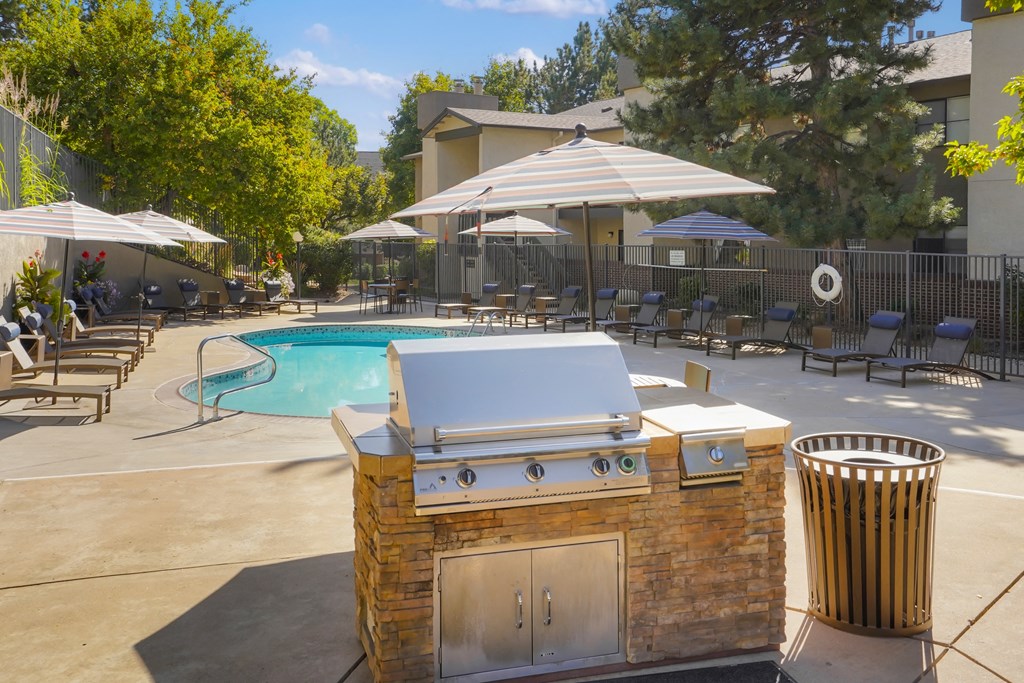 a gas grill is next to a swimming pool with umbrellas