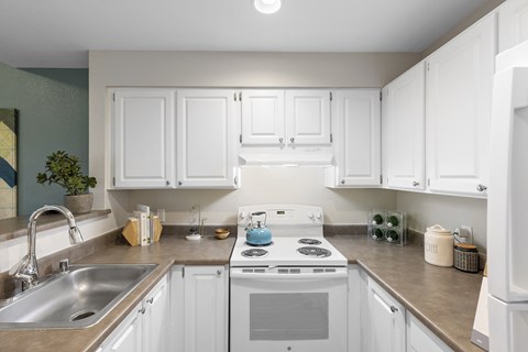a kitchen with white cabinets and a white stove and sink