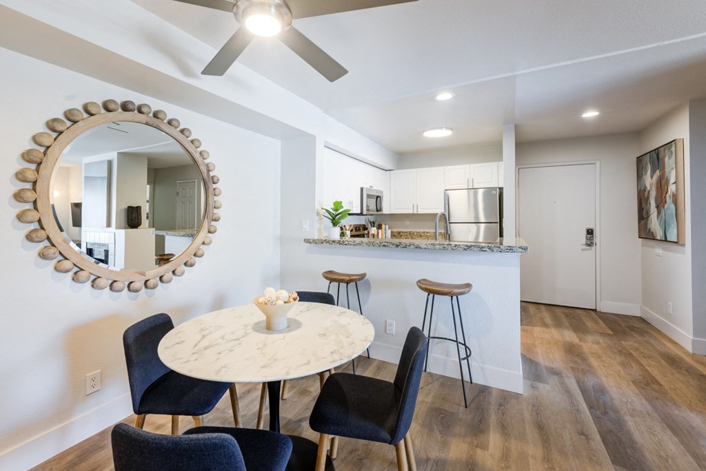 a dining area with a round table and four chairs and a kitchen in the background