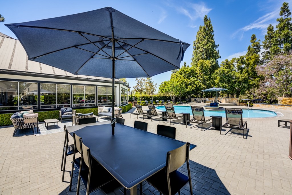 a patio with a dining table and chairs and a pool in the background