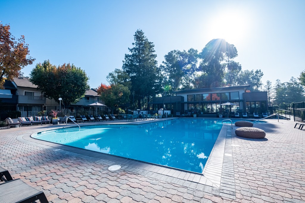 a swimming pool with lounge chairs and umbrellas in front of a building