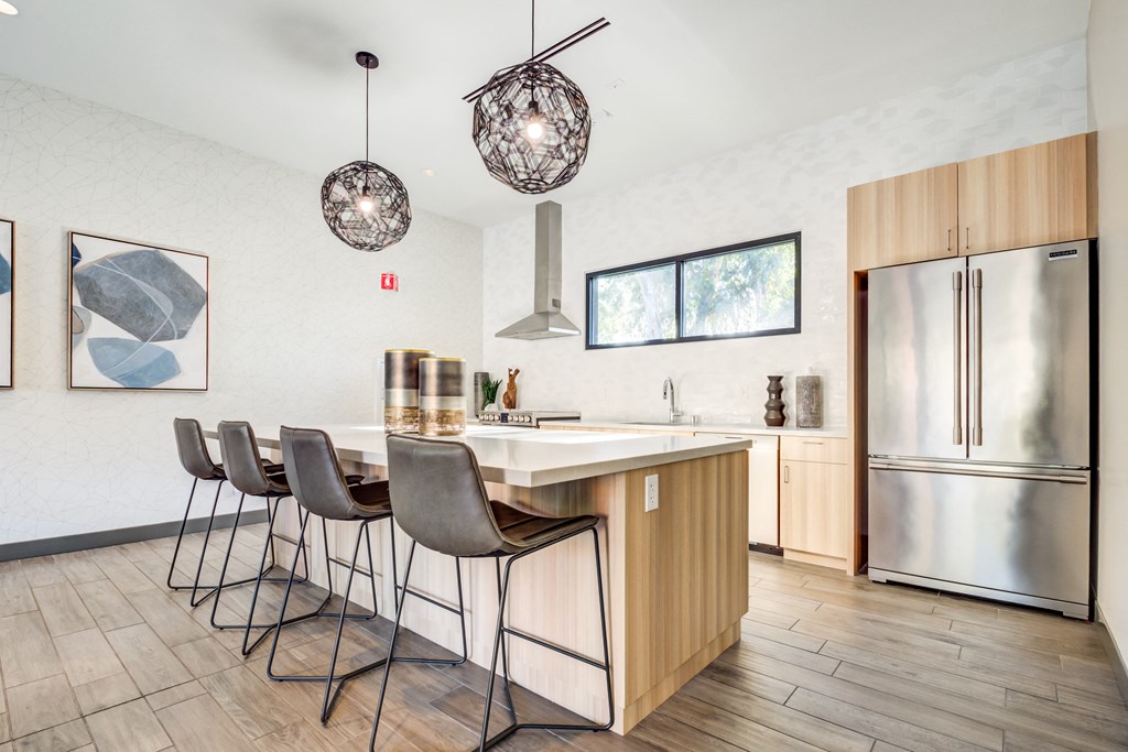 a kitchen with a large island with stools and a stainless steel refrigerator