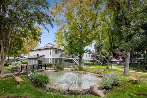 A house with a grey roof is surrounded by a garden with a pond and benches.