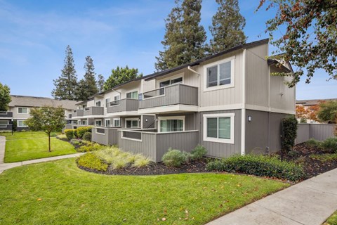 A modern apartment building with a well-maintained lawn and trees in the background.