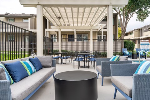 A patio with a white pergola and blue cushions.