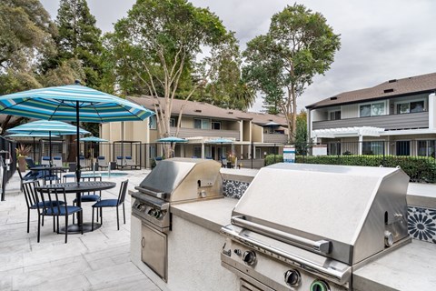 A BBQ grill is in the foreground of a patio with chairs and tables.