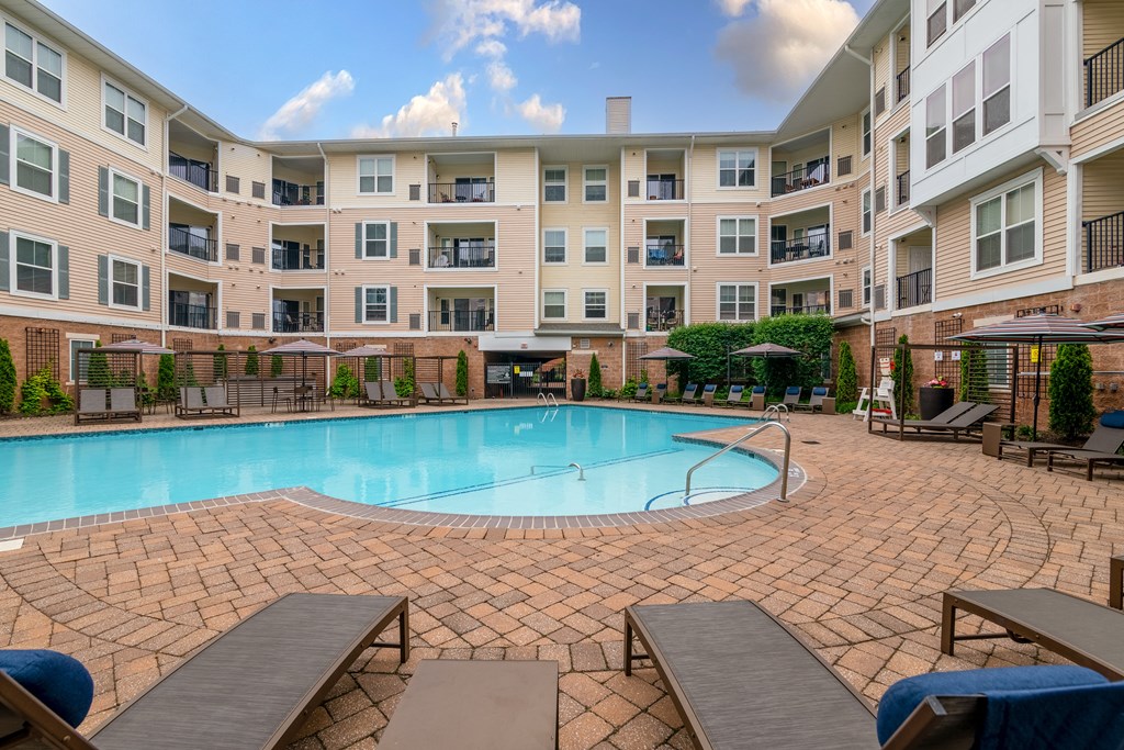 a swimming pool with lounge chairs and umbrellas in front of an apartment building