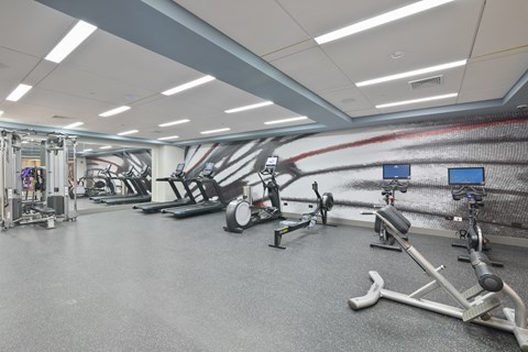 a gym with exercise equipment and a white wall with an abstract painting