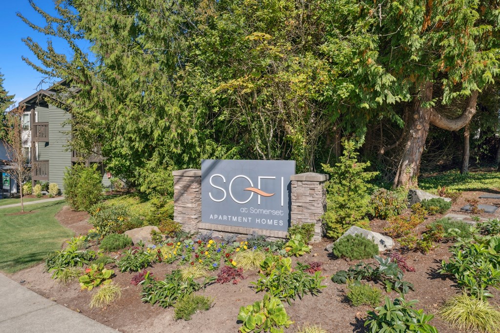 A sign for SCF Apartment Homes is surrounded by flowers and greenery.