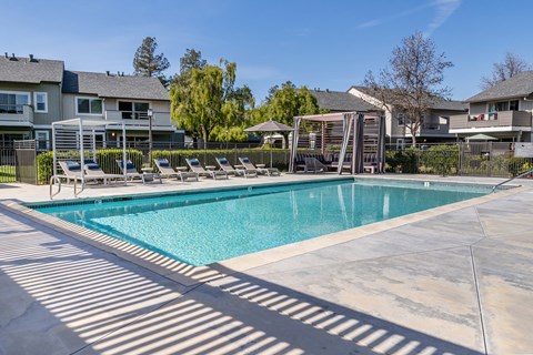 A large swimming pool surrounded by lounge chairs and apartment buildings.