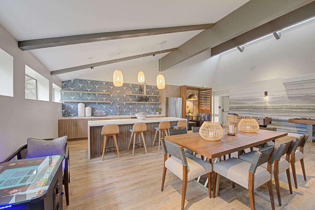 a dining area in the clubhouse with a wooden table and chairs and a kitchen in the background