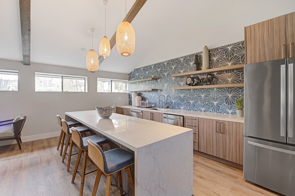 a clubhouse kitchen with a large white island with a marble countertop and a row of wooden cabinets