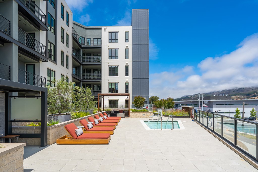 a pool with red lounge chairs on a rooftop terrace of an apartment building
