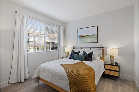 A bedroom with a large bed and a window with white curtains.