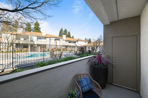 A balcony with a chair and a potted plant overlooks a pool and apartment buildings.