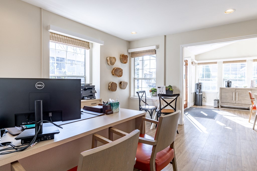 a desk with a computer and chairs in a room with a kitchen and a living room