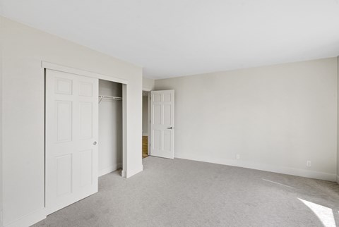 an empty living room with white walls and doors to a closet