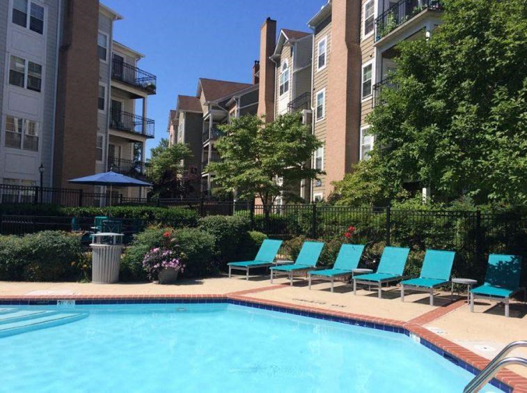 a swimming pool with blue chairs in front of an apartment building