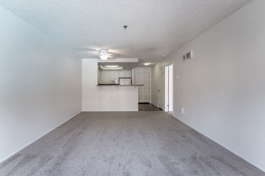 an empty living room with a kitchen in the background