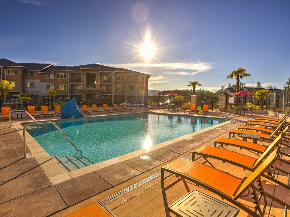a swimming pool with yellow chairs and a building in the background