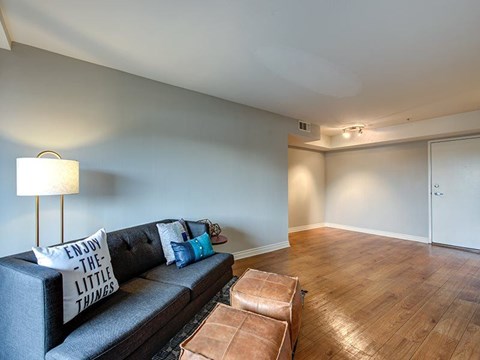 A living room with a grey couch and a brown leather ottoman.